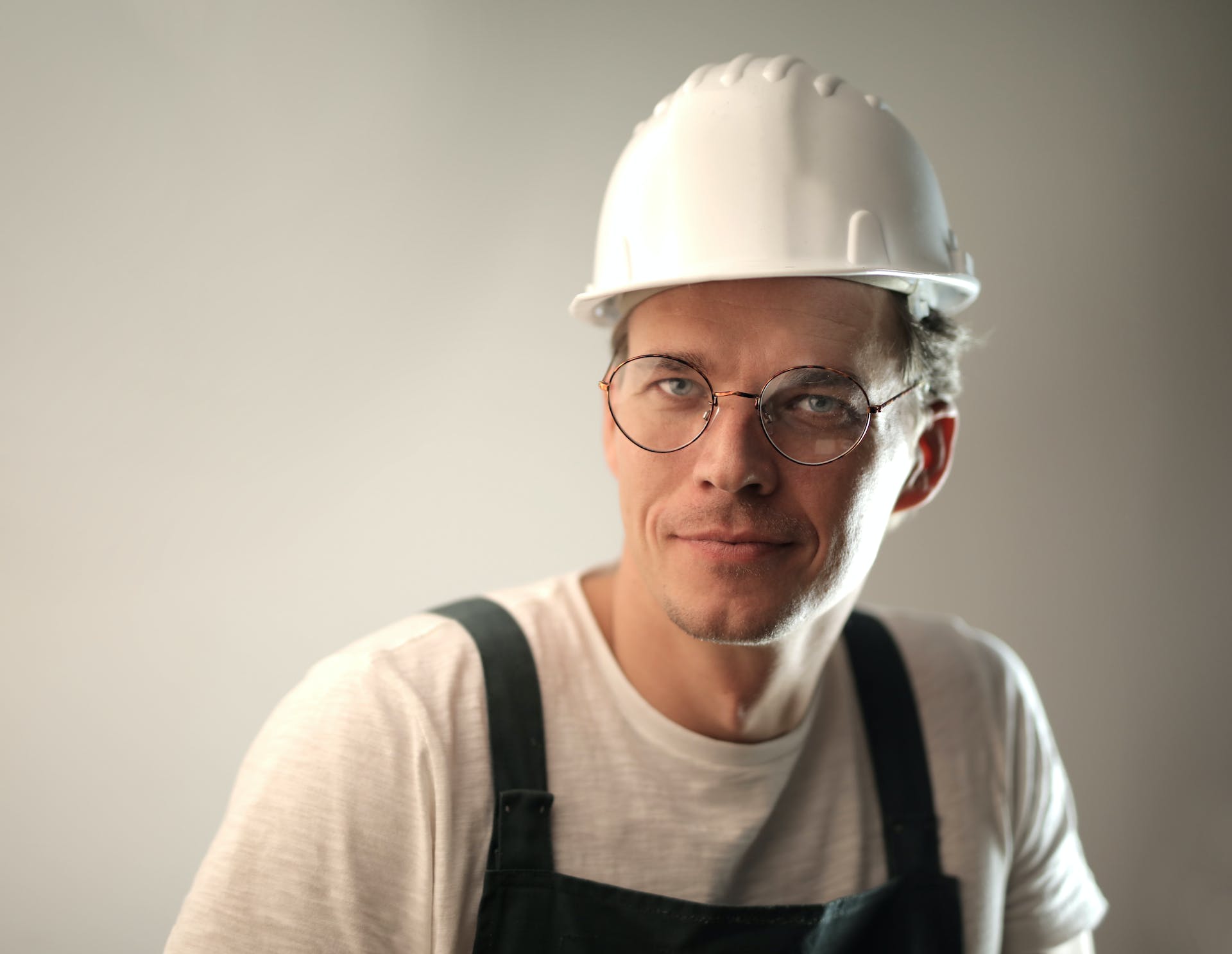 Content male builder in workwear and hardhat smiling on gray background in studio and looking at camera